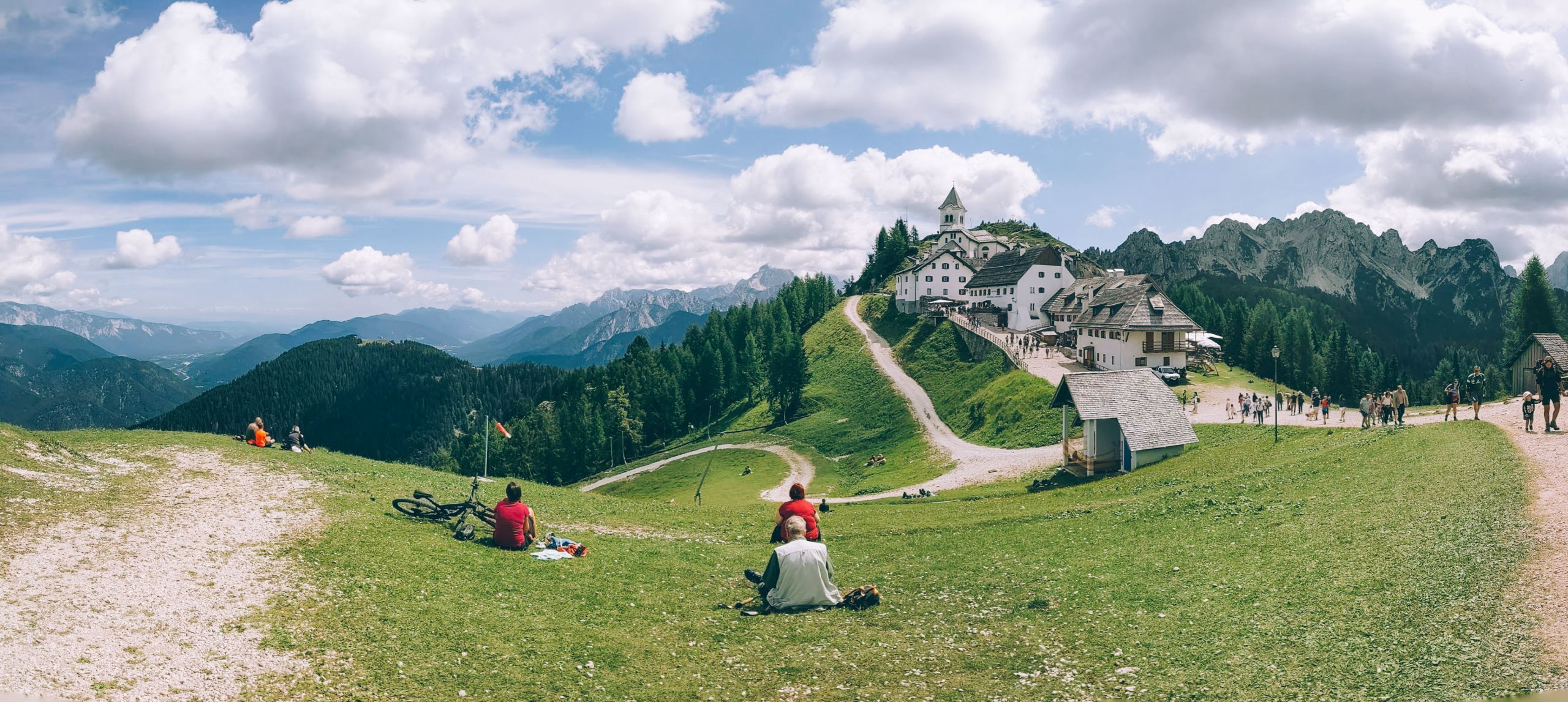 Ciclisti ed escursionisti su prato verde con vista sul Monte Santo di Lussari, Alpi Giulie, Tarvisio.